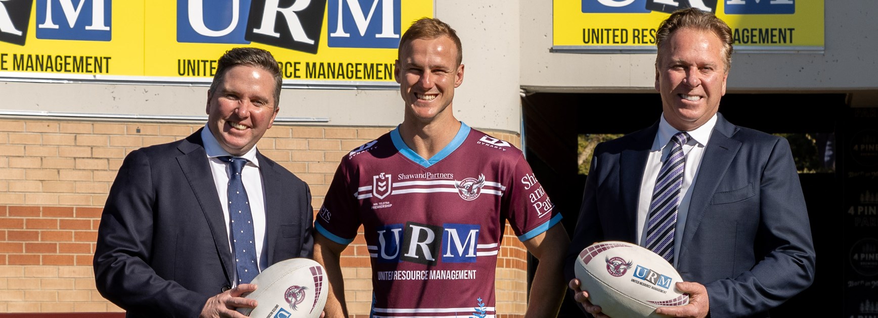 Daly Cherry-Evans models the 2022 URM Community Jersey with URM Managing Director, Anthony Johnston (right) and URM CEO, David Johnston (left).